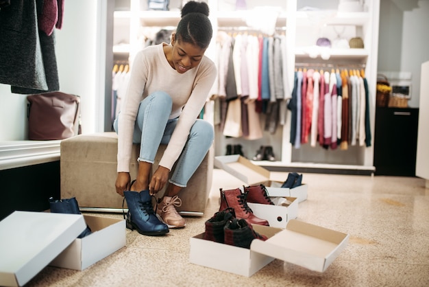 Persona di sesso femminile nera che prova sulle scarpe. maniaco dello shopping nel negozio di abbigliamento, stile di vita consumistico, moda