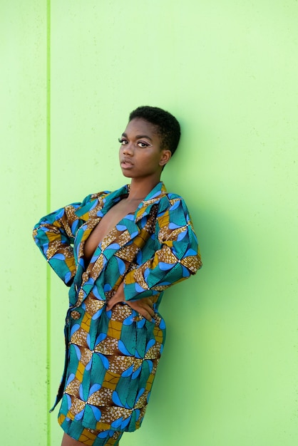 Black female in traditional African piece of fabric looking at camera against pistachio background