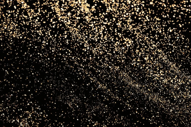 Black festive background. Abstract scattering of gold sparkles on black. Holiday backdrop, selective focus.