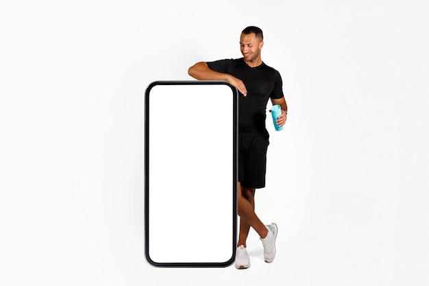 Black fitness man standing near big mobile phone white background