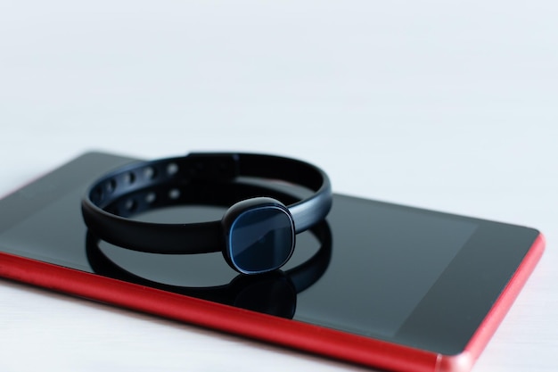 Black fitness tracker on red smartphone over white background