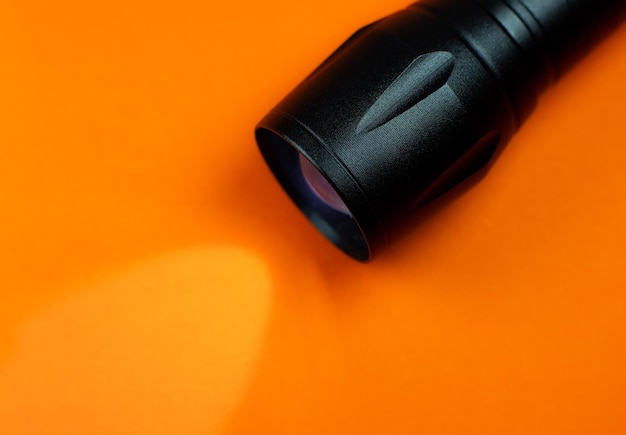 Black Flashlight and a ray of light on the orange background. Close up photo.