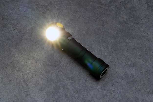 A black flashlight with a lit flash on the ground.