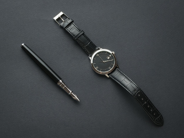 Black fountain pen and black men's watch with hands on a black background. Subjects for men.