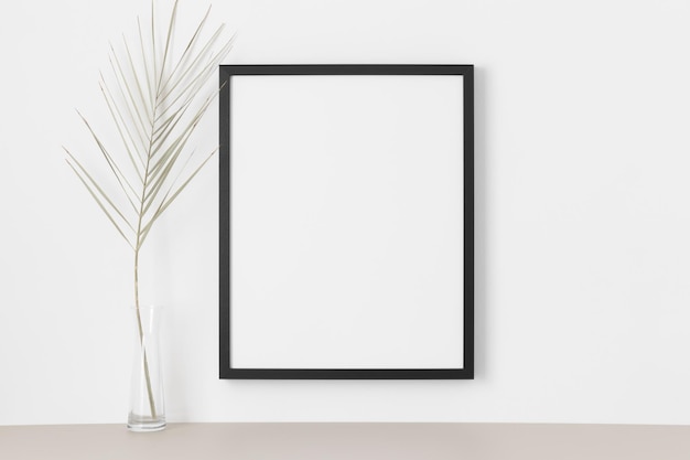 Black frame mockup on the wall with a palm leaf