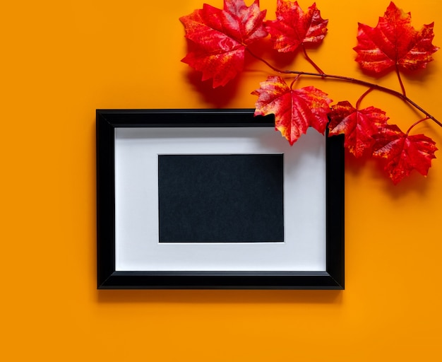  black frame with maple branches on orange background. Autumn concept. Place for text.