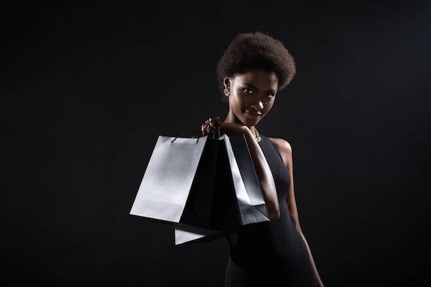 Photo black friday concept african american woman hold black shopping bags on black background