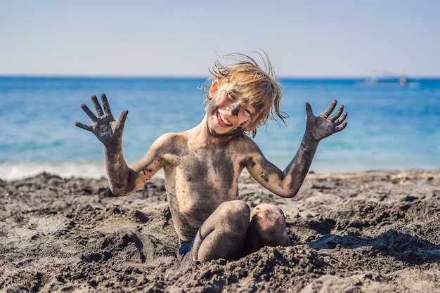 Black friday concept lachende jongen met vuil zwart gezicht zittend en spelend op het zwarte zandstrand van de zee