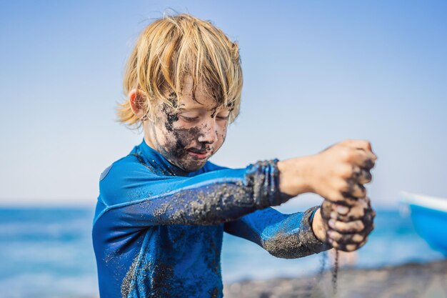 Black friday concept smiling boy with dirty black face sitting and playing on black sand sea beach