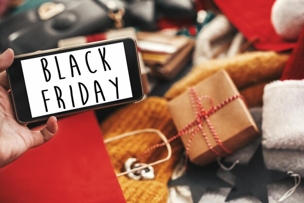 Black friday grote verkooptekst op telefoonscherm speciale korting kerstaanbieding teken big sales hand met telefoon met reclameboodschap bij creditcards tassen kleding geschenken