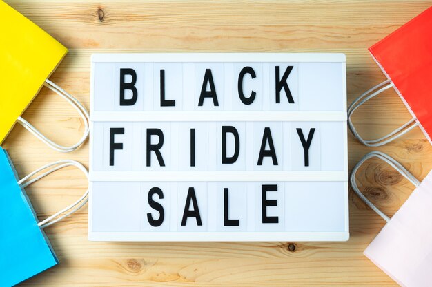 Black friday-inscriptie op lightbox op een houten tafel en papieren zakken. reclameconcept.