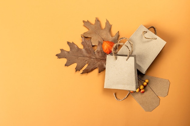 Black friday sale concept. shopping paper bags, handmade tags,\
fall oak leaves, autumn decor. light background, flat lay, top\
view