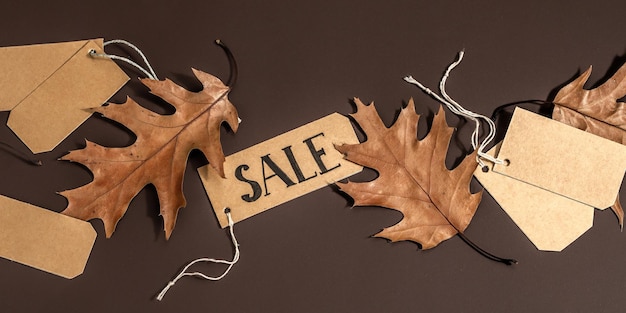 Foto vendita del black friday. etichette di carta, foglie d'autunno, concetto di shopping con sconti. sfondo marrone scuro, luce intensa alla moda, ombra scura, formato banner