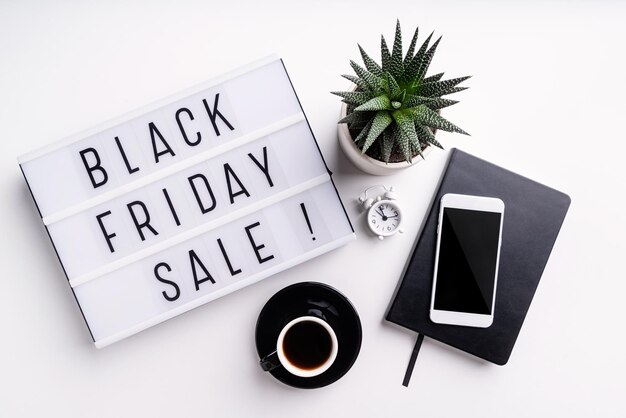 Black Friday Sale woorden op lightbox met kop koffie mobiele telefoon en potplant top view plat lag op witte achtergrond