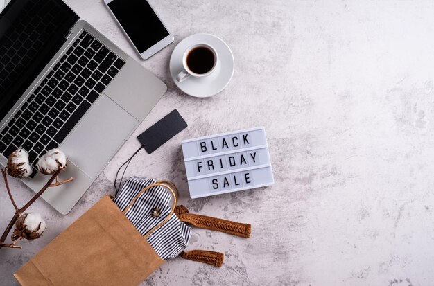 Photo black friday sale words on lightbox with cup of coffee laptop and shopping bag top view flat lay on white background