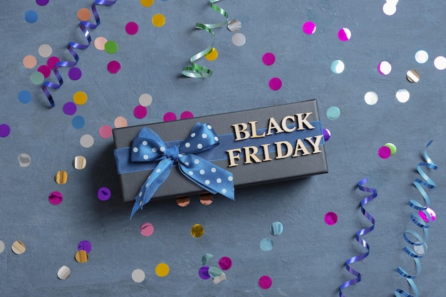 Foto black friday-tekst met cadeau en feestelijk klatergoud plat op donkere cementachtergrond