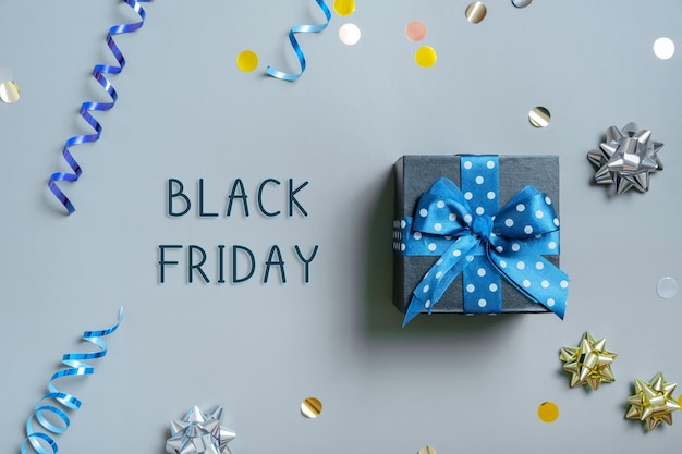 Black Friday text with gift box and festive tinsel flat lay on grey background Top view