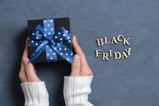 Black Friday text with gift in female hands flat lay on dark cement background Top view