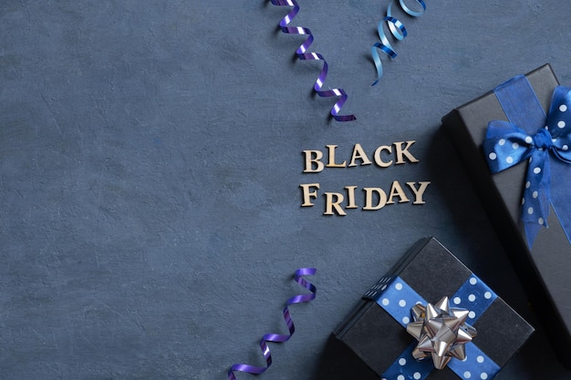 Black Friday text with gifts and holiday tinsel flat lay flat lay on dark cement background copy space Top view