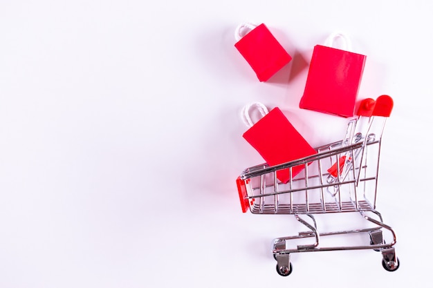 Black Friday . Trolley cart and red paper shopping bags on white . copyspace .