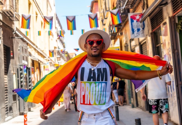 Черный гей ходит в солнцезащитных очках на вечеринке гордости с улыбающимся флагом лгбт