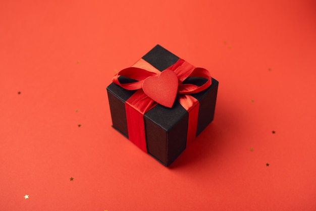 Black gift box tied with a red ribbon and red heart. Valentine's Day concept. with little stars.