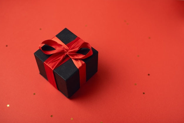 Black gift box tied with the red ribbon on red. Valentine's Day concept.