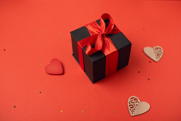 Black gift box tied with a red ribbon and wooden hearts with little stars. Valentine's Day concept.