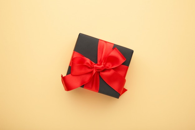 Black gift box with red ribbon and bow on beige .