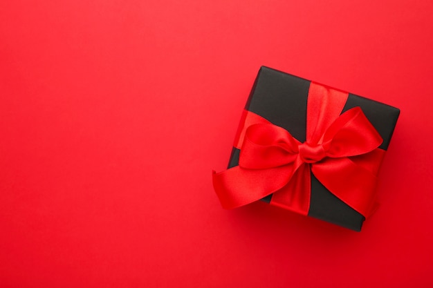 Black gift box with red ribbon and bow on red .