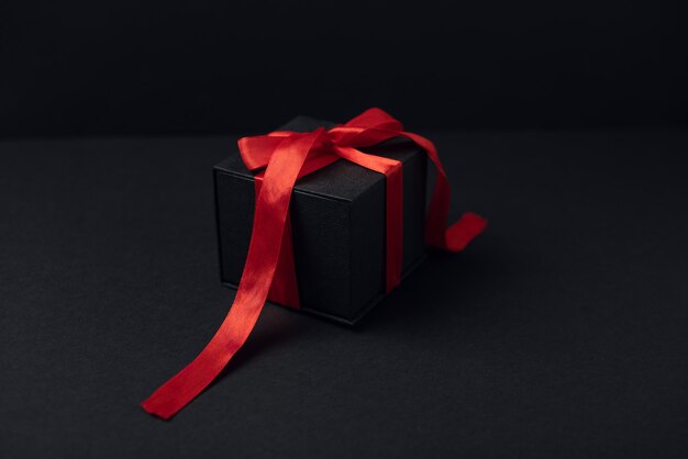 Black gift box with red ribbon on the dark surface.