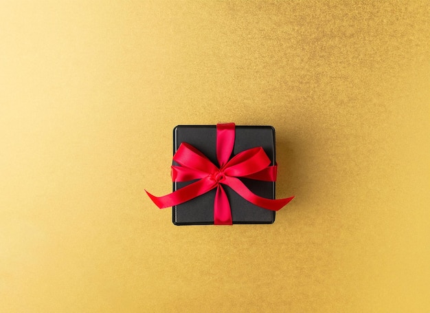 Black gift box with red ribbon on golden background with copy space