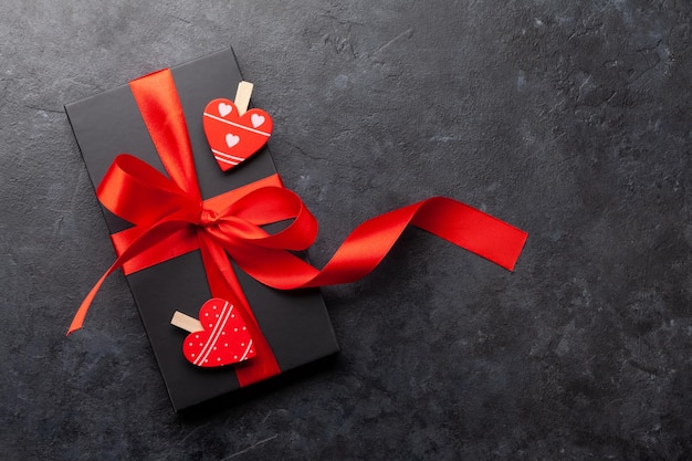 Black gift box with red ribbon on stone background Top view flat lay with copy space