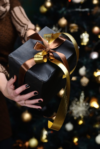 Black gift in the hands of a girl and fir-tree