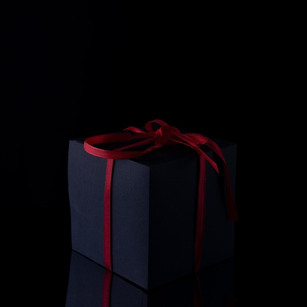 Black gift with red ribbon on black background