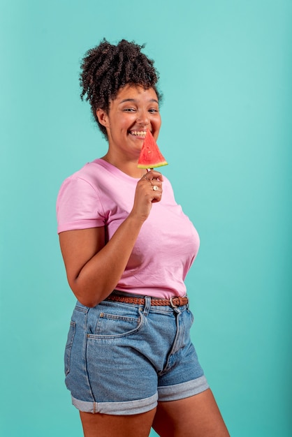 Black girl eating a slice of watermelon in the shape of ice cream on a turquoise background