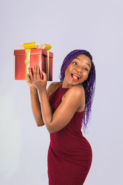 A black girl enjoys a Christmas red big gift. Girl smiles and receives gift.