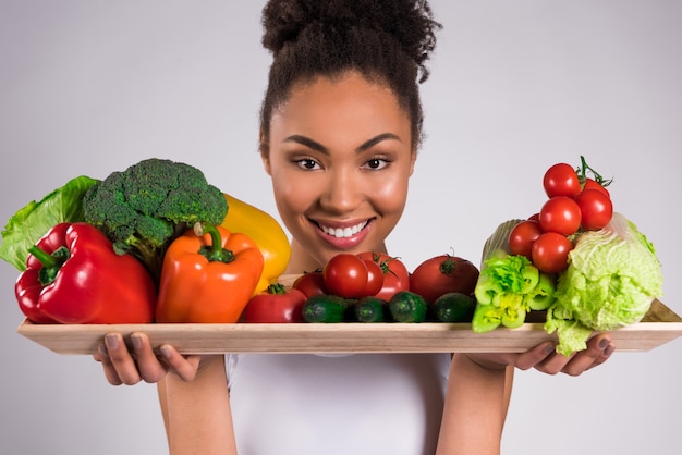 Black girl holding tray with vegetables isolated.