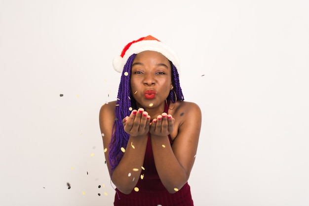 Black Girl in Santa Claus cap in festive red dress blow confetti 