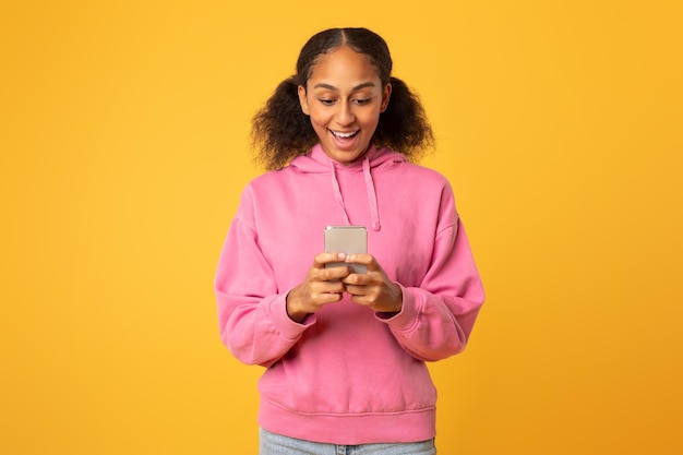 Black girl scrolling social media on smartphone over yellow backdrop