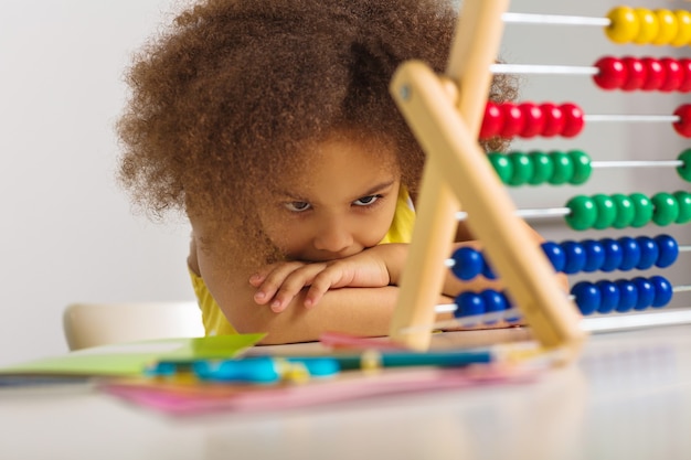 a black girl in a yellow dress is puzzled by an example of arithmetic girl portrait with abacus