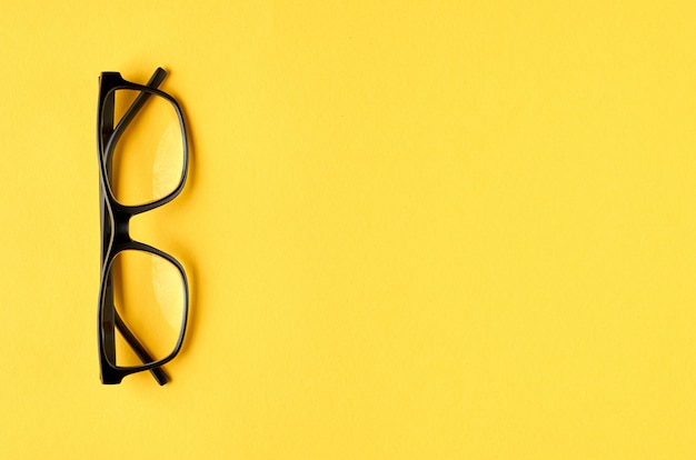 Black glasses on yellow surface, eyeglasses.