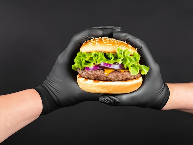 black glove hand holding a burger isolated on a black background