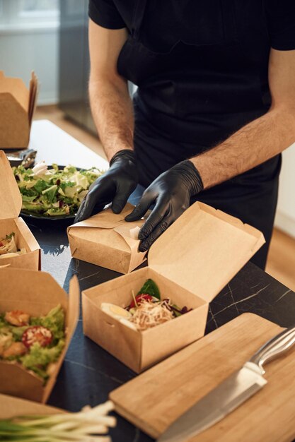 Photo in the black gloves man is packing food into the paper eco boxes indoors restaurant