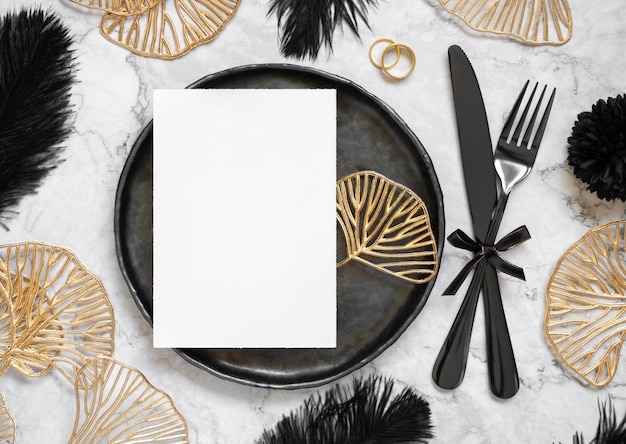 Photo black and golden wedding table setting with a blank card and rings top view mockup