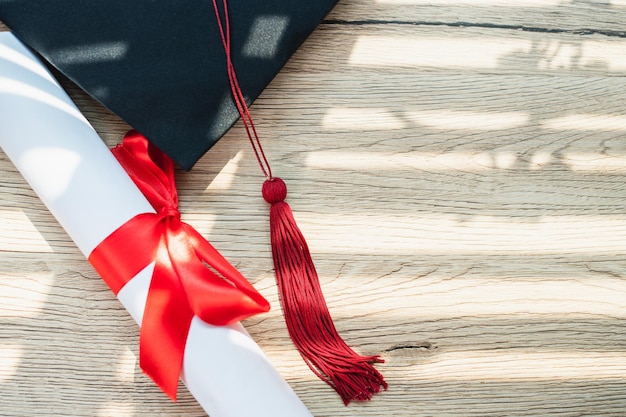 Foto un berretto di laurea nero e un certificato di laurea sono posti su uno sfondo di legno