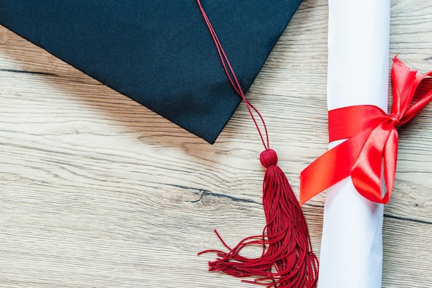 Foto un berretto di laurea nero e un certificato di laurea sono posti su uno sfondo di legno