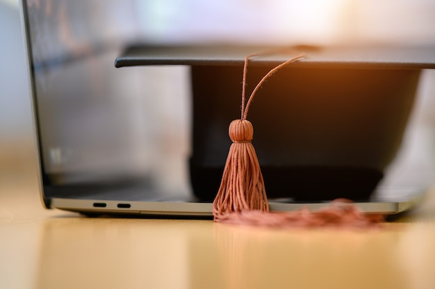 Black graduation cap placed on a laptop on a wooden table