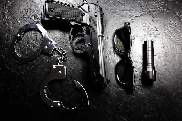 Photo black gun, flashlight, glasses and police metal real handcuffs lie on the black background. private detective work. searching information. crime and robbery, prison concept.