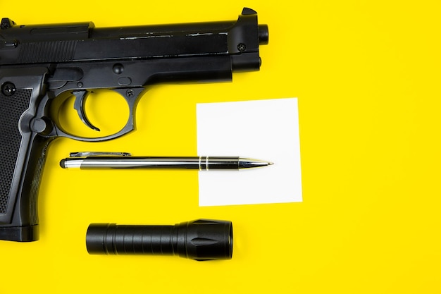 Photo black gun reminder note paper pen and flashlight lies on a yellow background private detectives work searching information concept